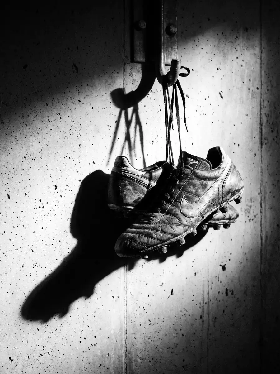 A pair of worn football boots hanging on a hook, black and white