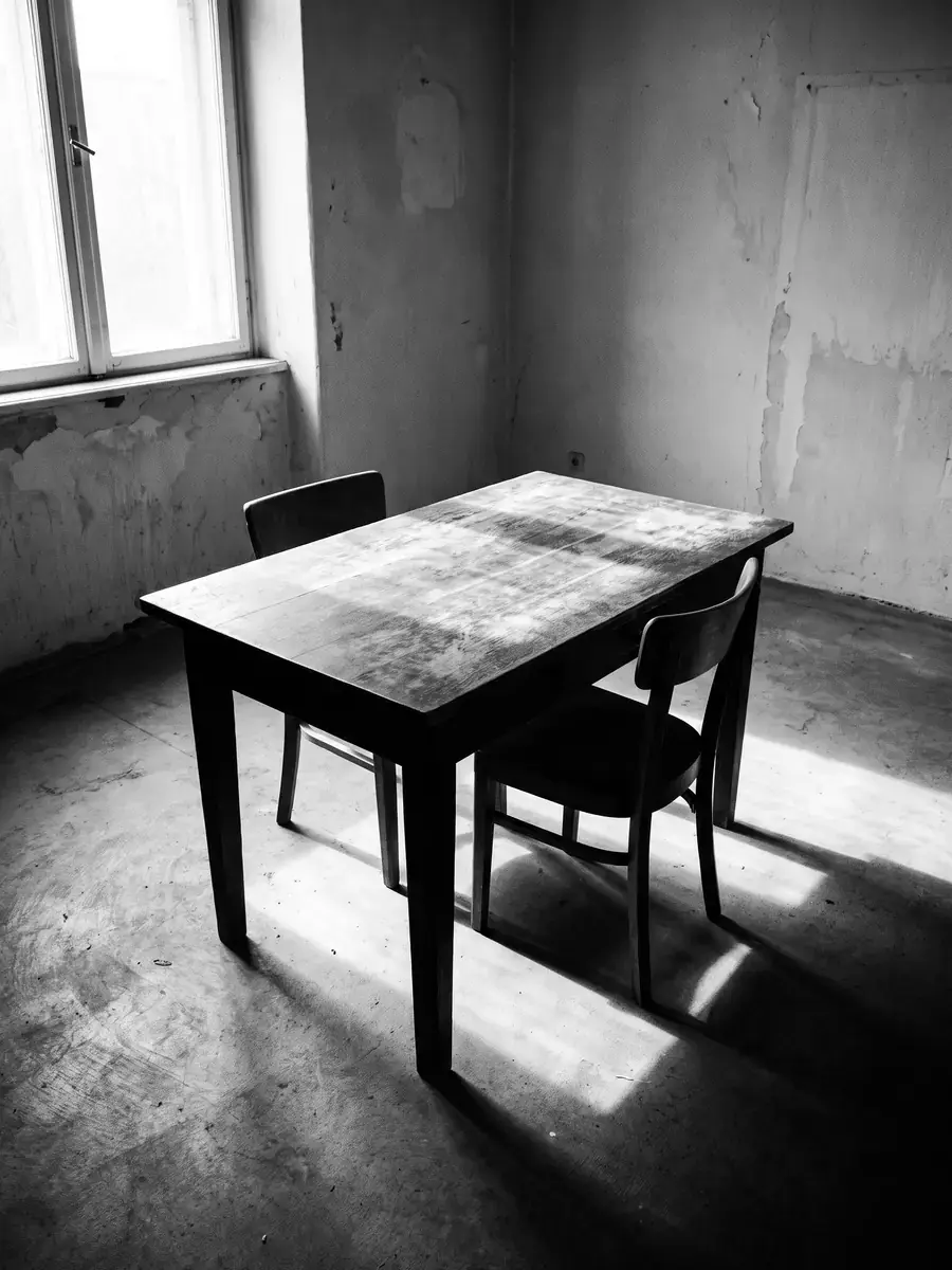 An empty table and two chairs in a bare room, black and white